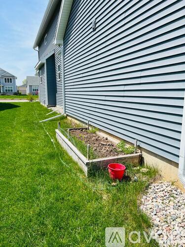 A red bucket sits on a grassy area next to a building.