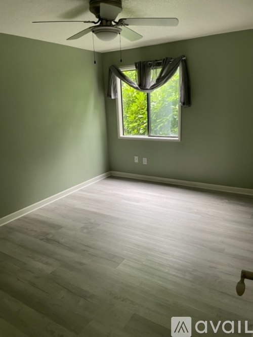 A room with a ceiling fan and a window with a view of trees.