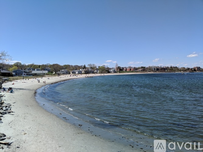 A beach with people walking on the sand and buildings in the distance.