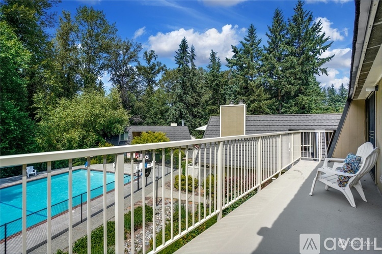 A balcony with a white railing overlooks a pool and trees.