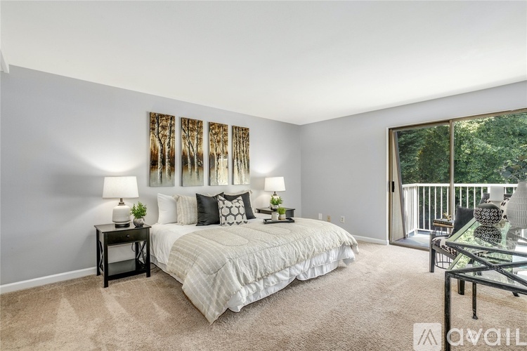A bedroom with a large bed, a nightstand, and a balcony overlooking trees.