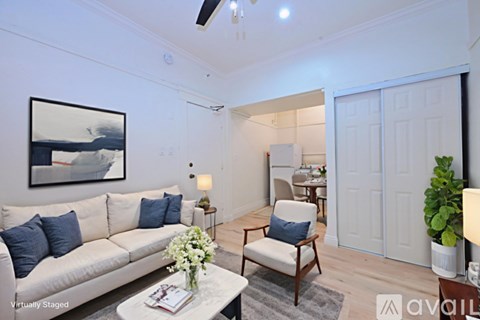A living room with a white couch, a painting on the wall, a small table with a vase of flowers, and a potted plant.