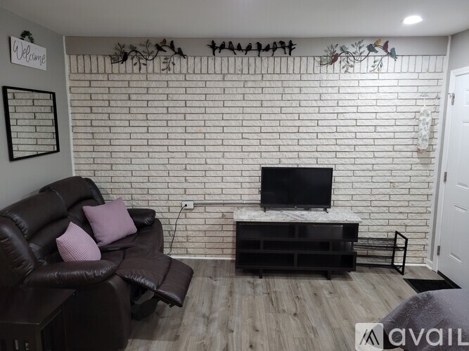 A living room with a brown leather couch and a white brick wall.