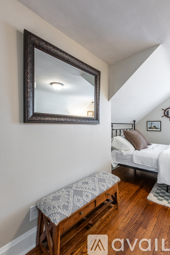 A mirror hangs on a wall above a bench in a bedroom.