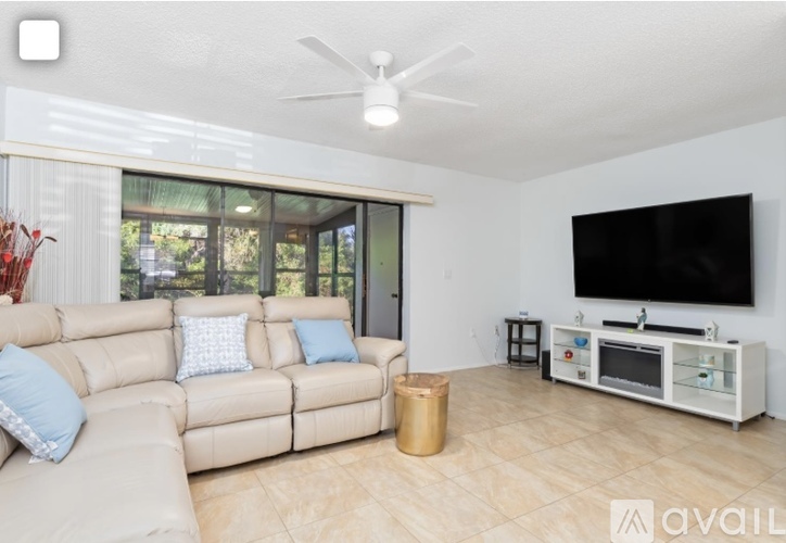 A living room with a beige couch, a flat screen TV, and a ceiling fan.