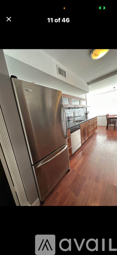 A stainless steel refrigerator in a kitchen with wooden flooring.