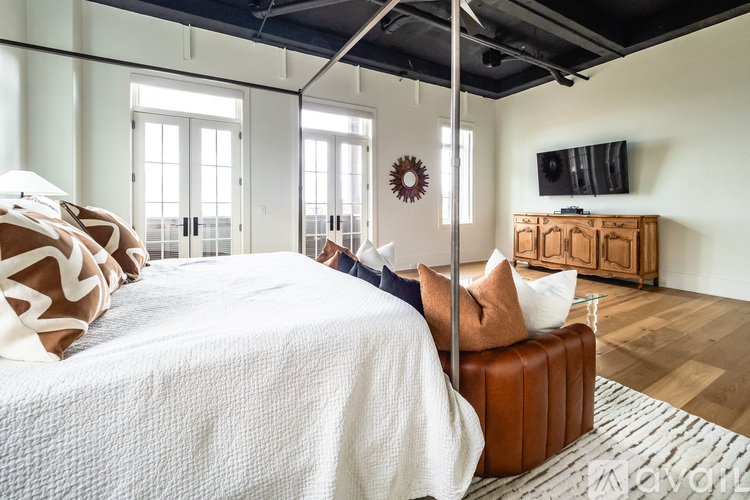 A bedroom with a white bedspread and a brown leather ottoman.