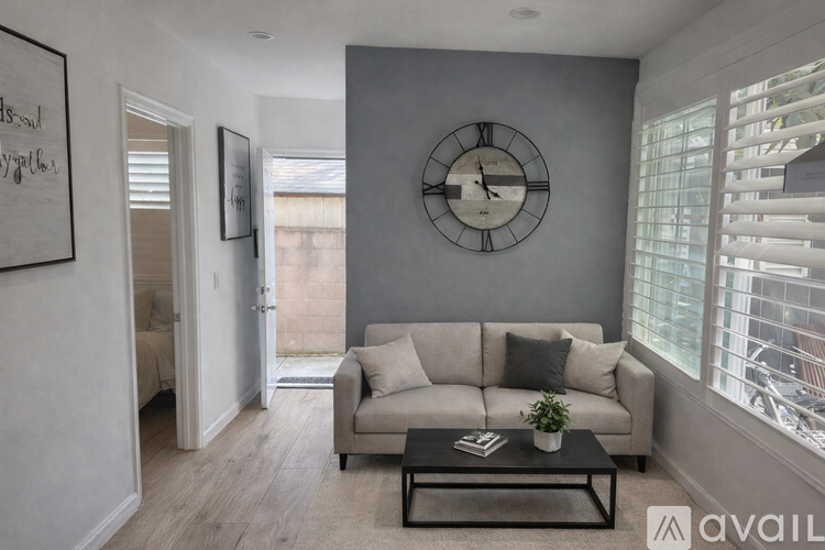 A living room with a grey couch, a black coffee table, and a large clock on the wall.