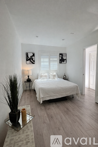A bedroom with a bed, nightstand, and a plant on a coffee table.