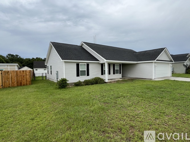 A house with a white exterior and a grey roof is surrounded by a grassy lawn.