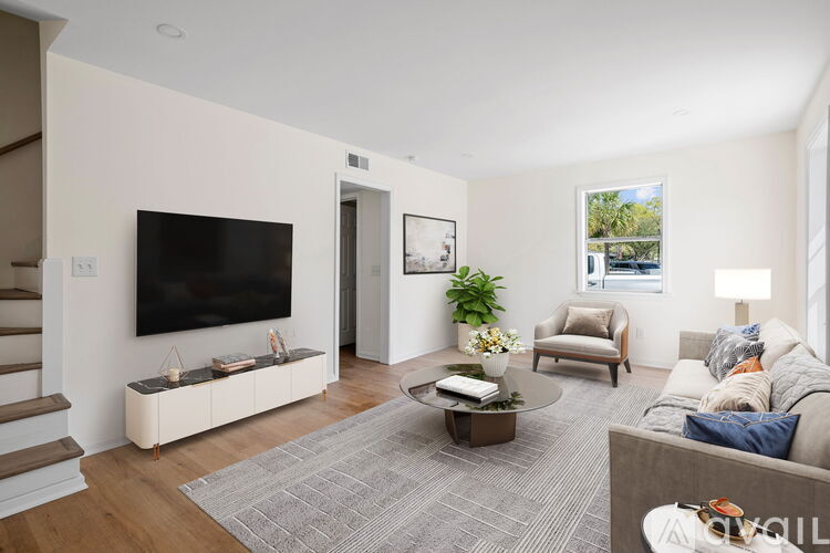 A living room with a grey sofa, a coffee table, a television, and a potted plant.