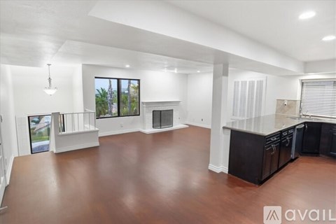 A spacious living room with a fireplace and a kitchen area with dark wood flooring.