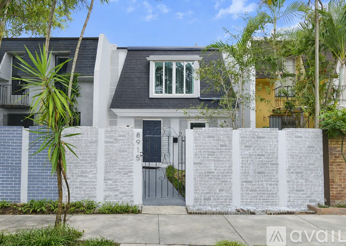 A modern house with a black roof and white walls is surrounded by a white fence and has a black gate.