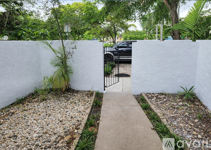 A white wall with a gate in the middle of a gravel path.