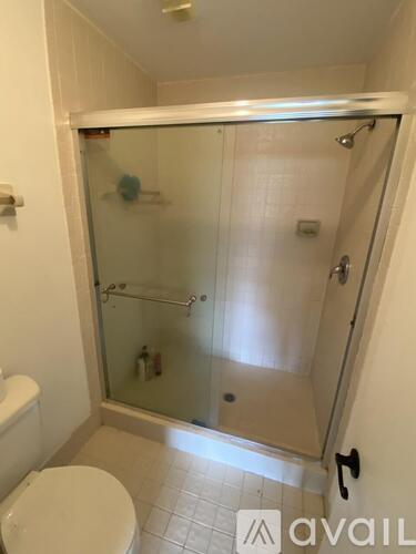 A white toilet is in a small bathroom with a glass shower stall.