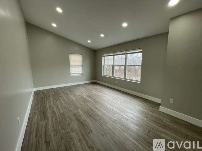 A spacious room with wooden flooring and two windows.