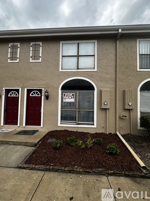 A beige house with a red door and a for sale sign.