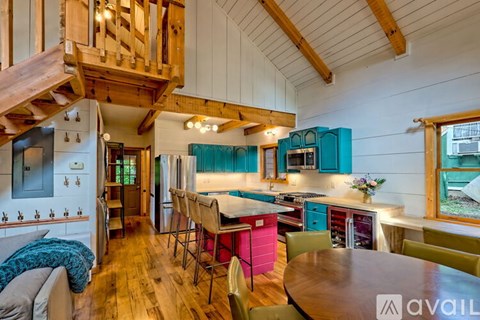 A wooden staircase leads to the upper level of a brightly lit kitchen with a table and chairs.