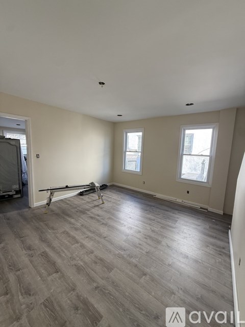 A room with wooden flooring and two windows.