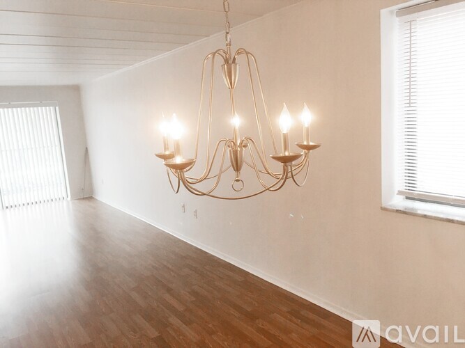 A chandelier with six lights hangs from the ceiling in a room with wooden floors and white walls.