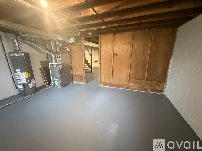A room with a concrete floor and walls, wooden door, and a staircase in the background.