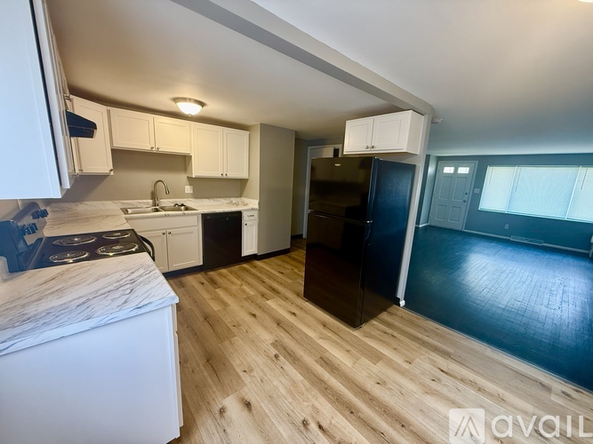 A kitchen with a black fridge and wooden floors.