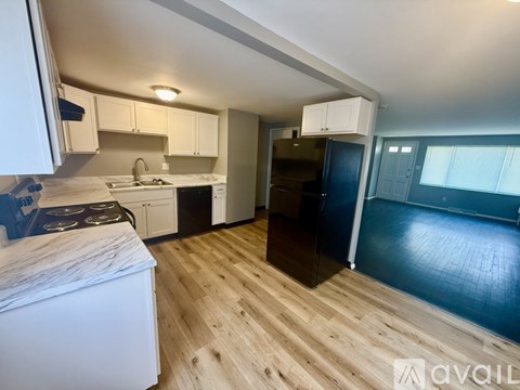 A kitchen with a black fridge and wooden floors.