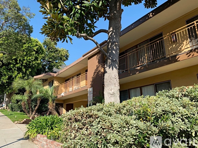 A tree trunk is in the foreground of a building with balconies.