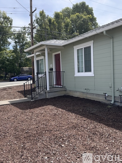 A small house with a red door and a blue car parked in front.