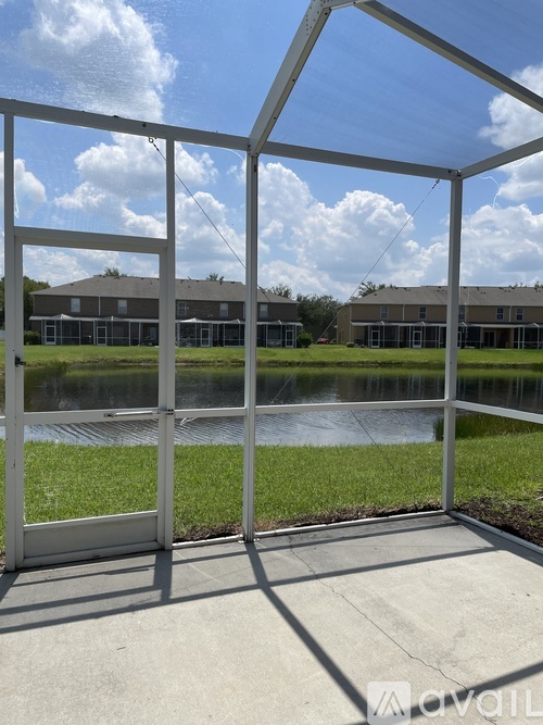 A white metal structure with a glass door is in the foreground of a sunny day with a pond and buildings in the background.