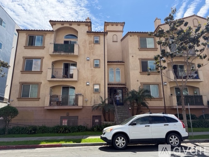 A white SUV is parked in front of a tan building with balconies.