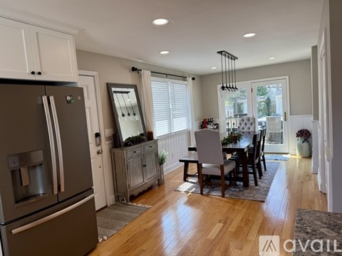 A kitchen with a refrigerator, a dining table with chairs, and a window with blinds.