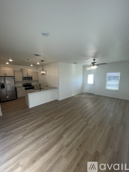 A spacious room with wooden flooring and a kitchen area in the background.