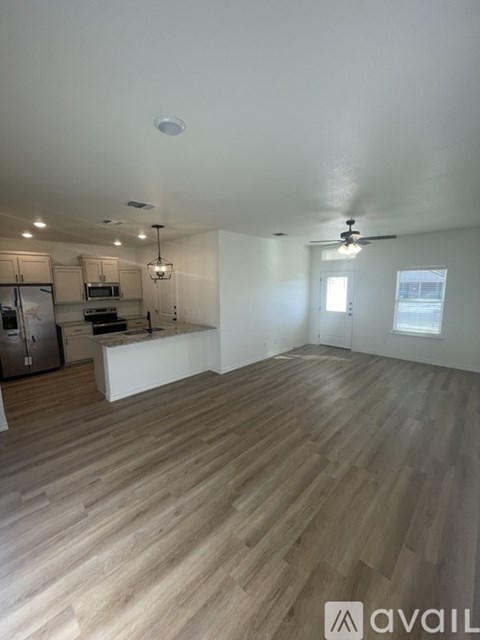 A spacious room with wooden flooring and a kitchen area in the background.