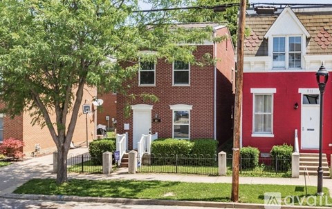 A red brick house with a white door and a tree in front.