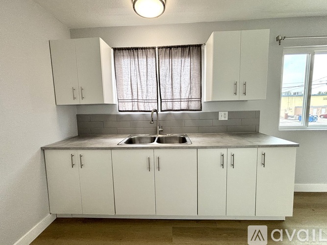 A kitchen with white cabinets and a window with curtains.