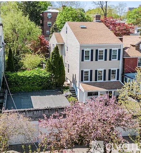 A white house with a brown roof is surrounded by trees and bushes.