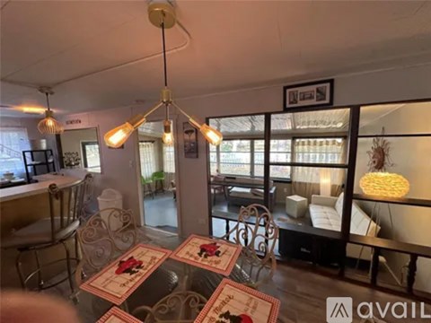 A living room with a glass table and chairs, a hanging light fixture, and a framed picture on the wall.