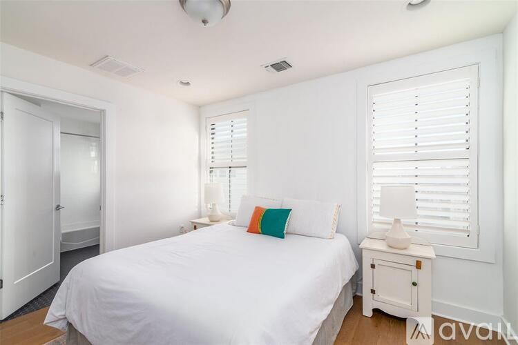 A bedroom with a white bed, a white nightstand, and a window with white blinds.