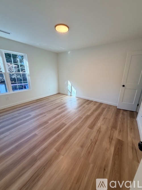 A room with wooden flooring and a window showing trees outside.