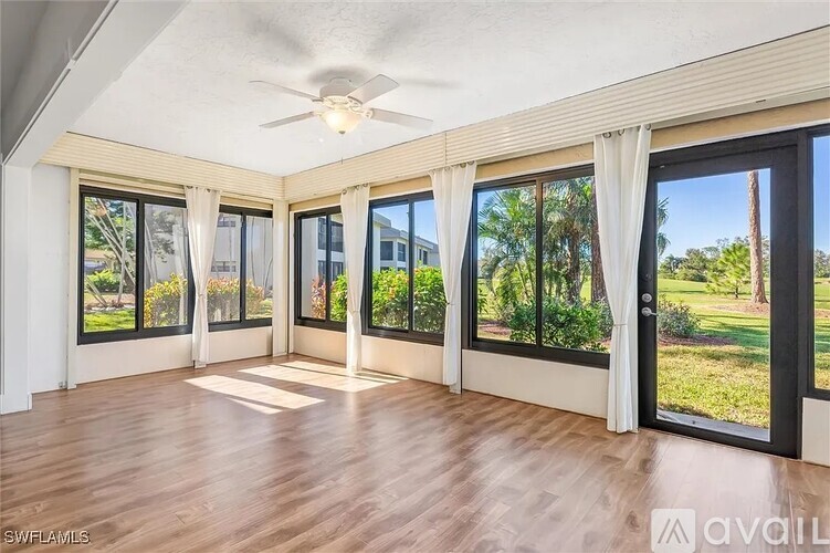A spacious room with wooden floors and large windows overlooking a garden.