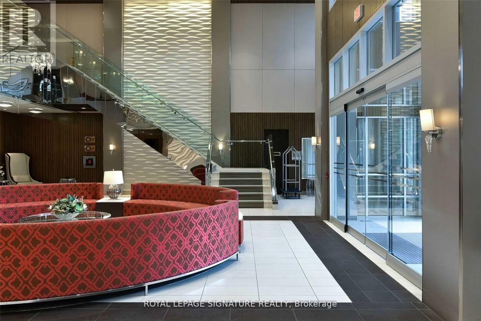 A red patterned sofa sits in a spacious lobby with a staircase and glass doors.