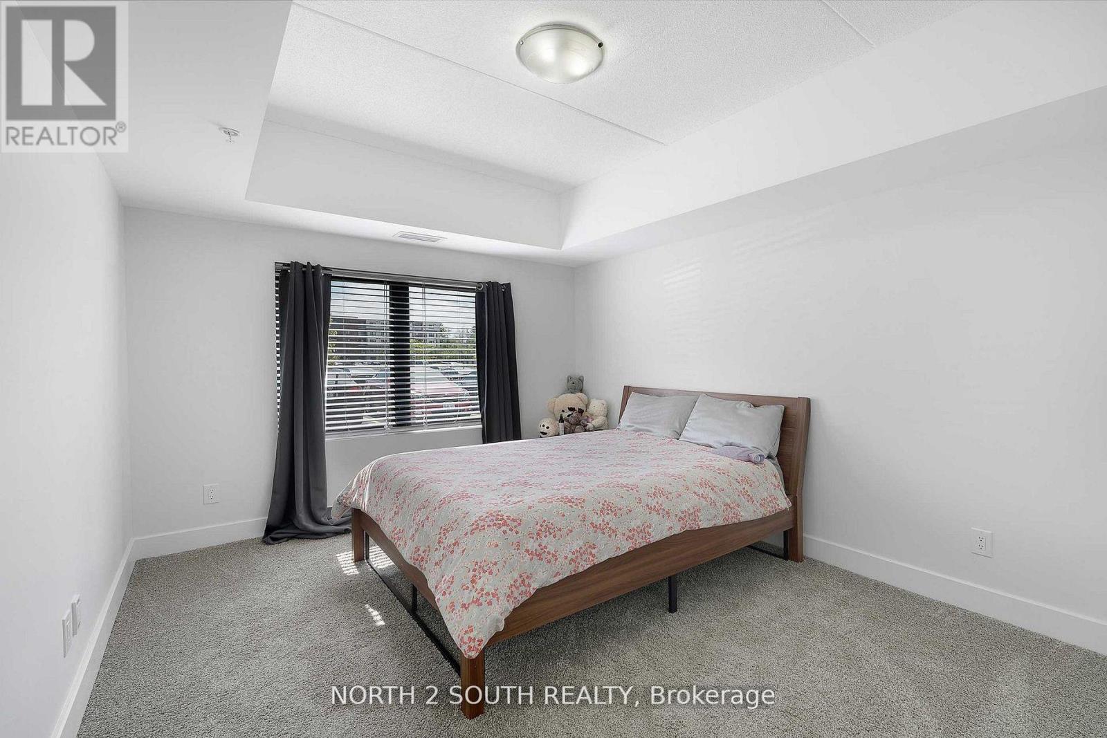 A bedroom with a bed, a window with curtains, and a carpeted floor.