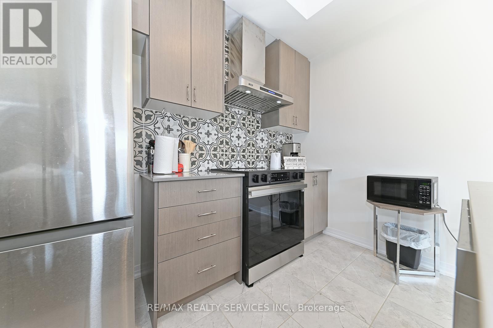 A kitchen with a stainless steel refrigerator, a microwave on a counter, and a range hood above the stove.