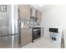 A kitchen with a stainless steel refrigerator, a microwave on a counter, and a range hood above the stove.
