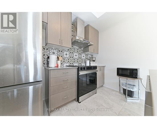 A kitchen with a stainless steel refrigerator, a microwave on a counter, and a range hood above the stove.