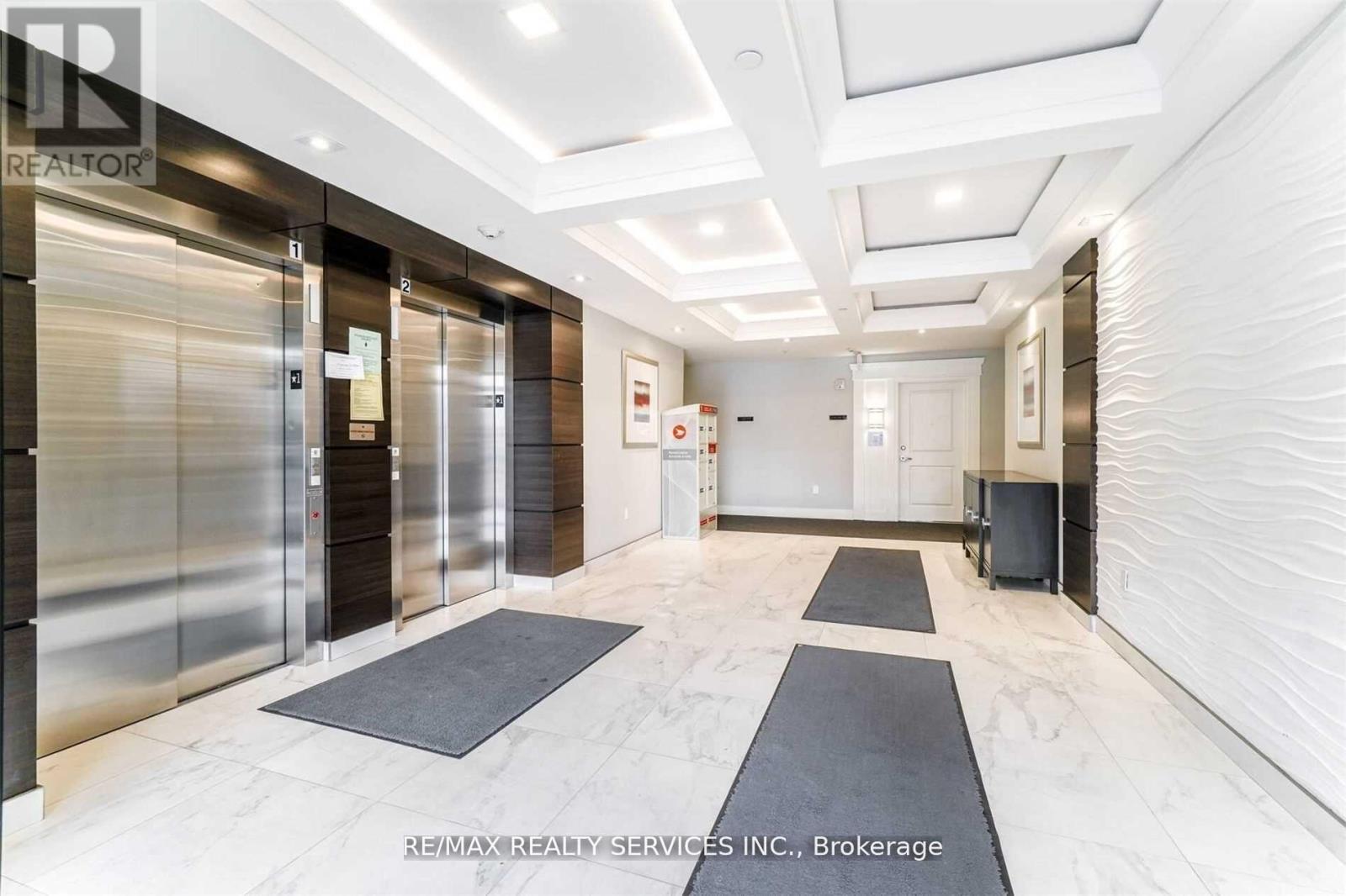 A hallway with a black and white rug in front of a glass elevator.