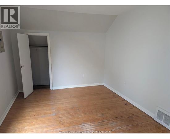A room with wooden floors and white walls, with a doorway leading to another room.