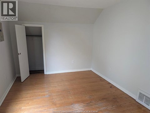 A room with wooden floors and white walls, with a doorway leading to another room.