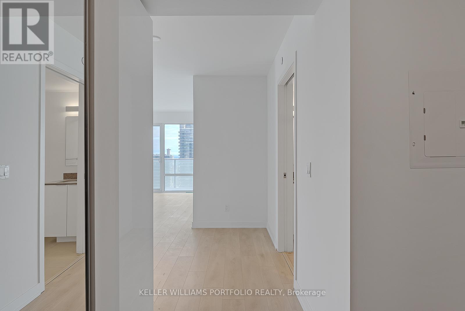 A white hallway with a door on the right and a kitchen in the background.